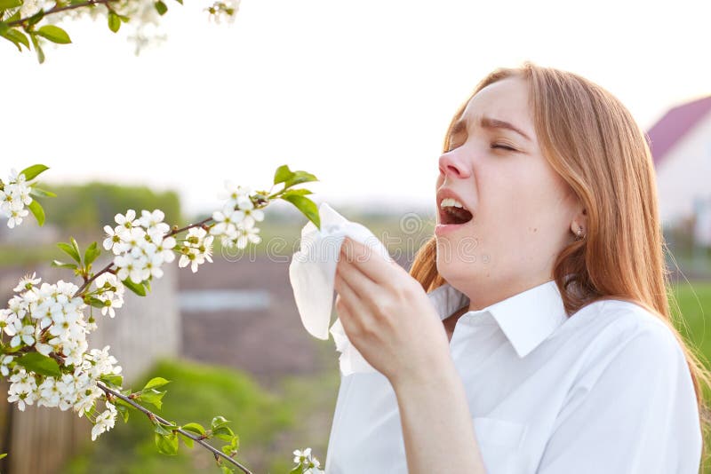 Allergiesymptomen De ontstemde jonge vrouw gebruikt weefsel, niest al tijd, bevindt zich dichtbij bloesem tijdens de lentetijd, d