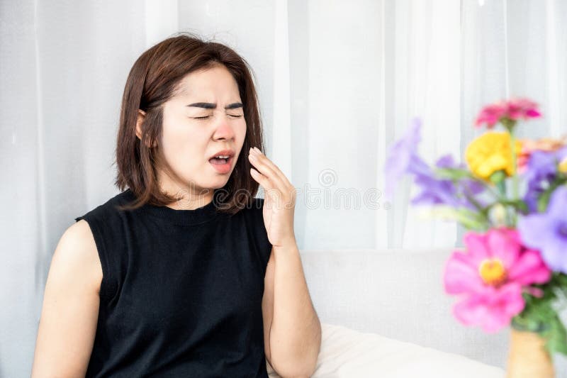 allergic Asian woman suffer from pollen allergy symptoms sneezing and has runny nose with bloom flower in living room. allergic Asian woman suffer from pollen allergy symptoms sneezing and has runny nose with bloom flower in living room