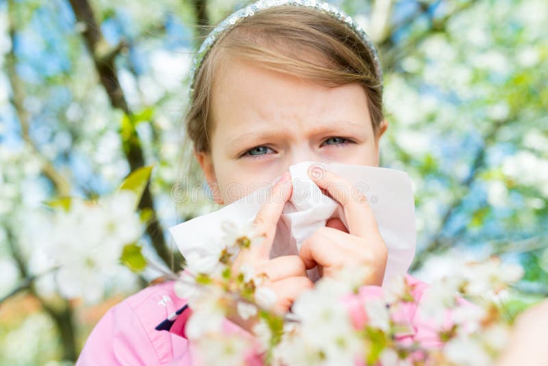 Allergy. Little girl is blowing her nose near spring tree in bloom - sneezing girl. Child with a handkerchief