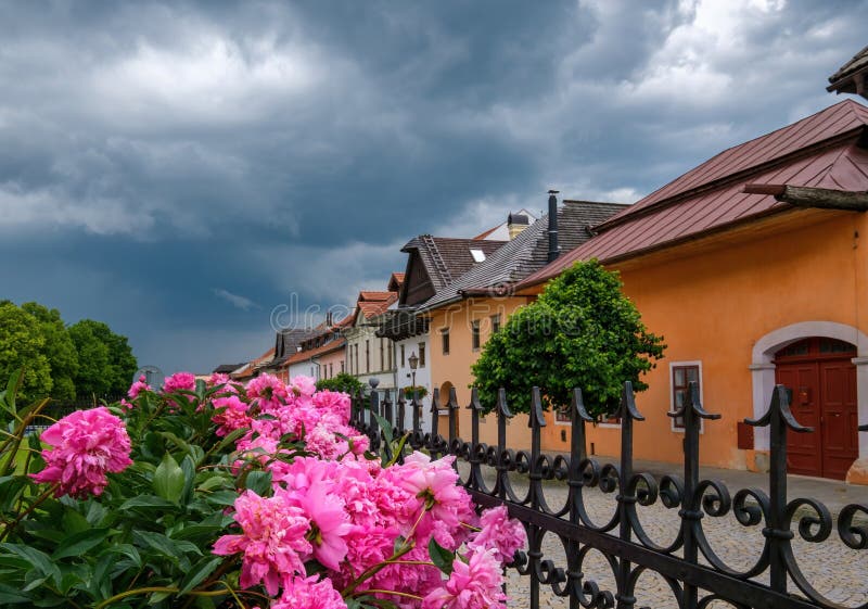 Ulička se starými historickými budovami a letní zahrádkou s květinami a bouřkovými mraky. Spišská Sobota, Poprad, Slovensko.