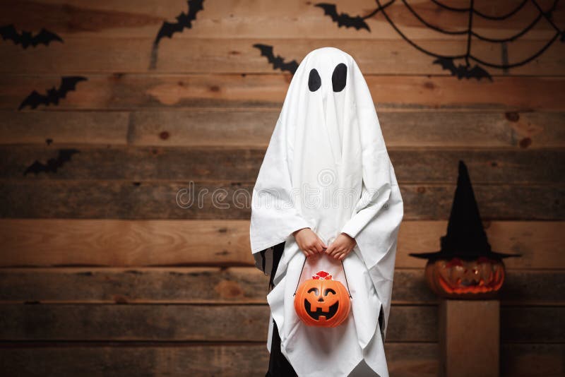 Allhelgonaaftonbegrepp - liten vit spöke med kruset för halloween pumpagodis som gör trick eller fest med krökta pumpor över slag fotografering för bildbyråer Allhelgonaaftonbegrepp - liten vit spöke med kruset för halloween pumpagodis som gör trick eller fest med krökta pumpor över slag fotografering för bildbyråer