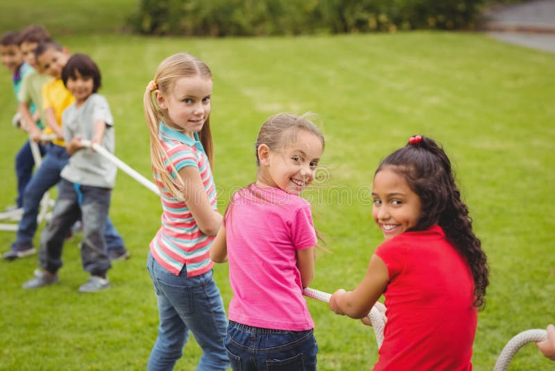 Cute pupils playing tug of war on the grass outside on elementary school campus. Cute pupils playing tug of war on the grass outside on elementary school campus