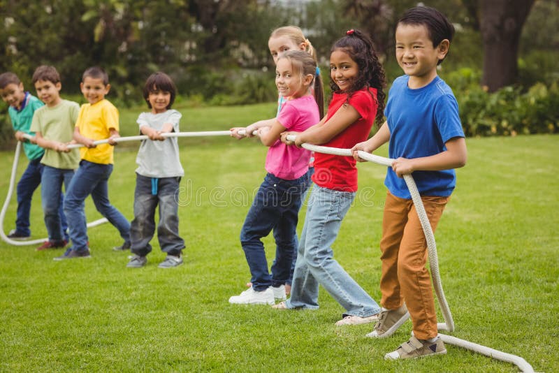 Cute pupils playing tug of war on the grass outside on elementary school campus. Cute pupils playing tug of war on the grass outside on elementary school campus