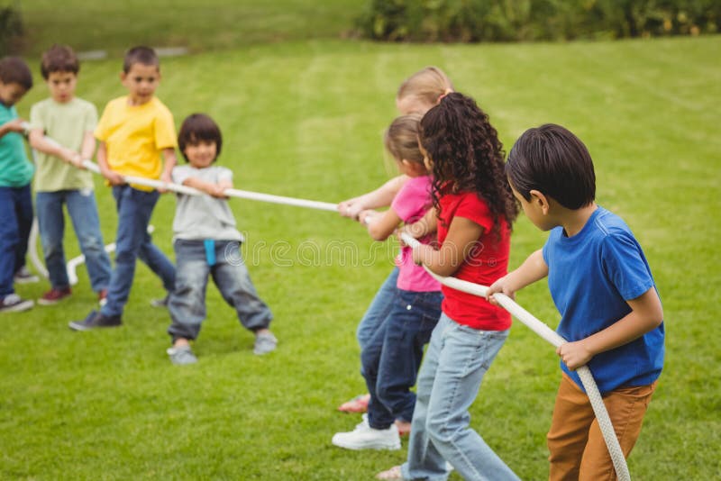 Cute pupils playing tug of war on the grass outside on elementary school campus. Cute pupils playing tug of war on the grass outside on elementary school campus