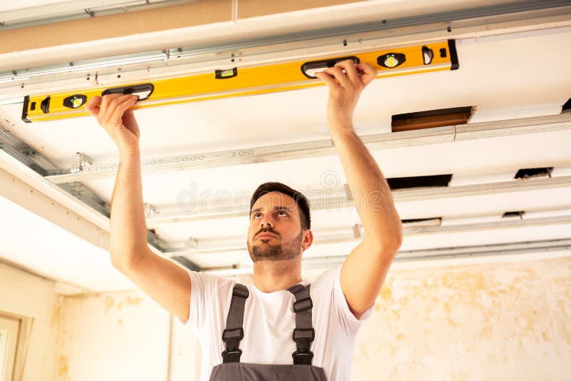 Alloggi il lavoratore del rinnovamento che controlla l'allineamento di un soffitto