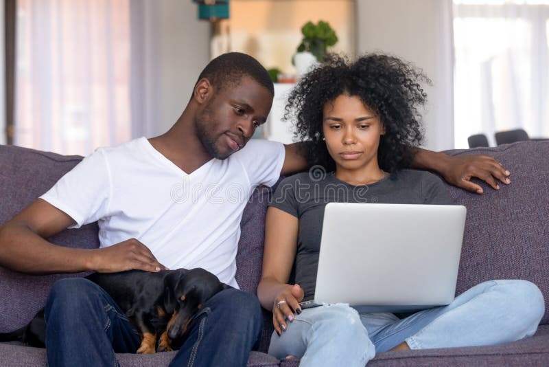 Allvarlig afrikansk amerikanman och kvinna som hemma använder bärbara datorn royaltyfri bild Allvarlig afrikansk amerikanman och kvinna som hemma använder bärbara datorn royaltyfri bild