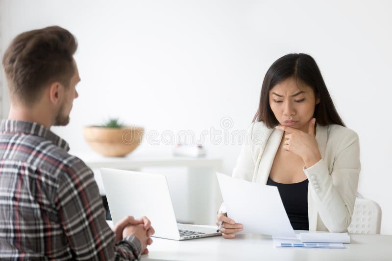 Allvarlig asiatisk arbetsgivare som läser CV som tvivlar i anställdcandidat fotografering för bildbyråer Allvarlig asiatisk arbetsgivare som läser CV som tvivlar i anställdcandidat fotografering för bildbyråer