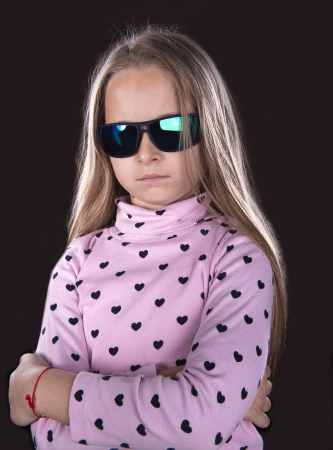 Allvarlig liten flicka som pockar i solglasögon i studion. Allvarlig liten flicka som i solglasögon i studio pockar över mörk bakgrund