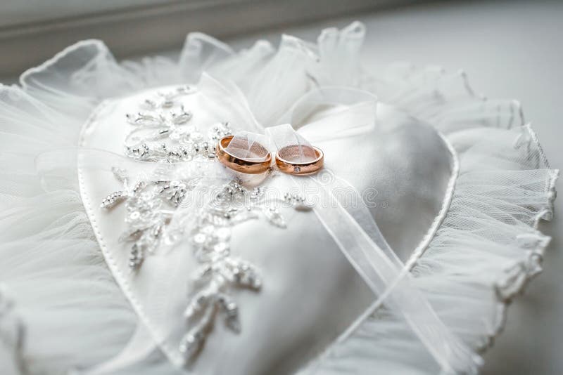 Heart-shaped white pillow with lace and wedding gold rings. Front side. Heart-shaped white pillow with lace and wedding gold rings. Front side