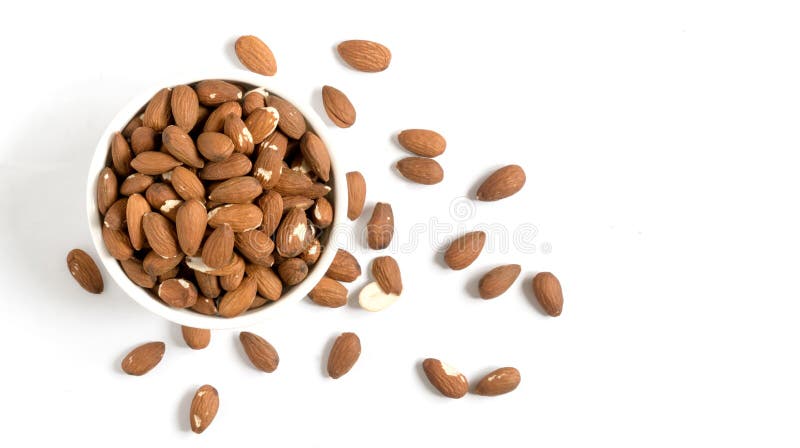Almonds in a bowl on white background. Some almonds around on the table. Isolated, top view. Almonds in a bowl on white background. Some almonds around on the table. Isolated, top view.