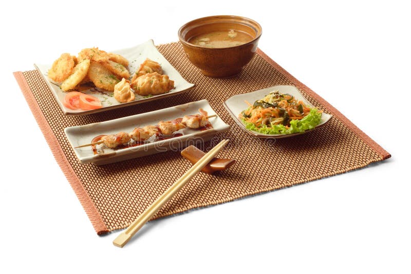 Asian lunch with salad, gedze, tempura, miso soup, kani sarada, yakitori tori and chopsticks on the matting over white background. Asian lunch with salad, gedze, tempura, miso soup, kani sarada, yakitori tori and chopsticks on the matting over white background