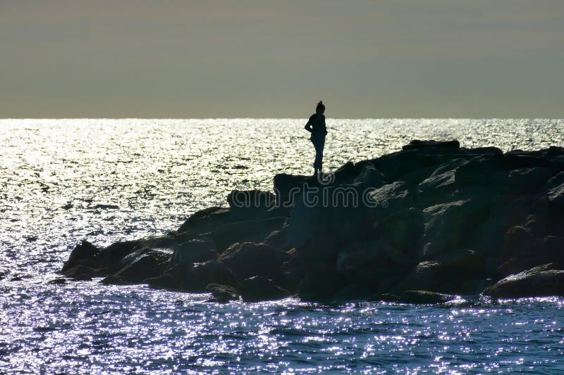 Alone female silhuette standing on cliff by the sea royalty free stock photo