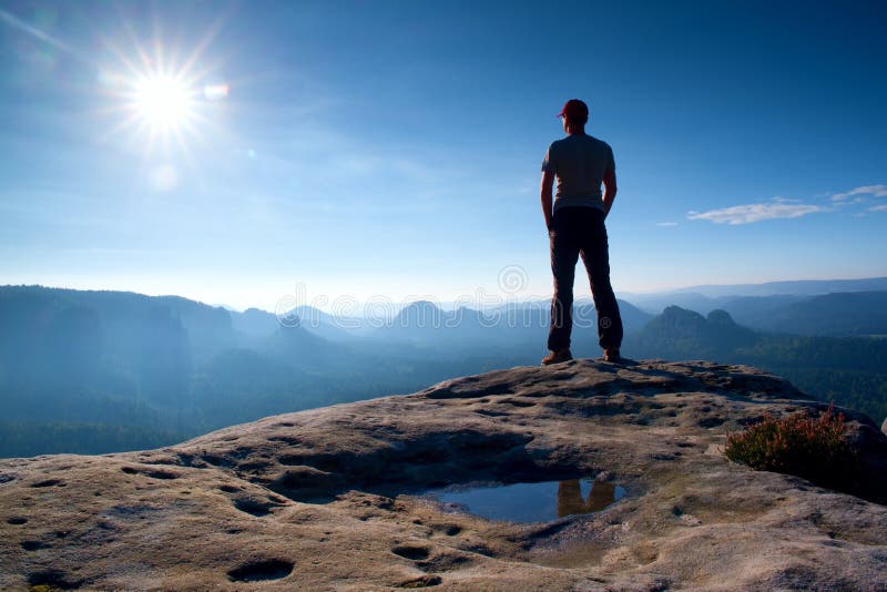 Alone man in red cap on peak of sharp peak in rock empires park and watching over the misty and foggy morning valley to Sun. Beaut