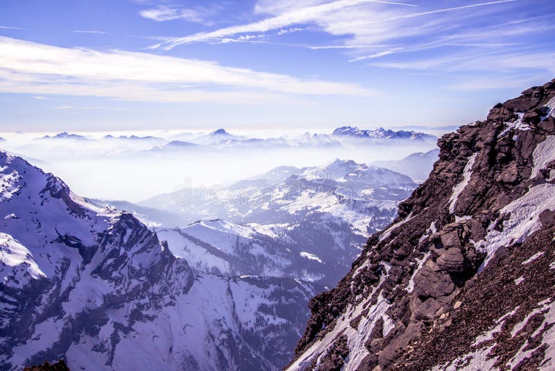 Snow covered mountains and rocky peaks in the fog in the Swiss Alps, over blue sky. Snow covered mountains and rocky peaks in the fog in the Swiss Alps, over blue sky