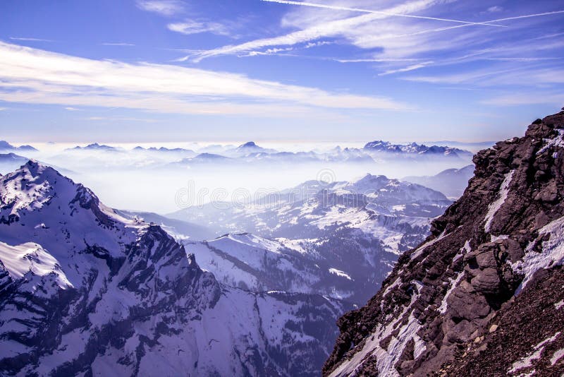 Snow covered mountains and rocky peaks in the fog in the Swiss Alps, over blue sky. Snow covered mountains and rocky peaks in the fog in the Swiss Alps, over blue sky