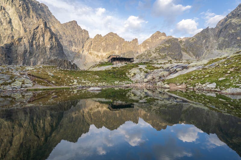 Alpská chata obklopená horami odráží v popředí tarn při východu slunce, slovensko, evropa