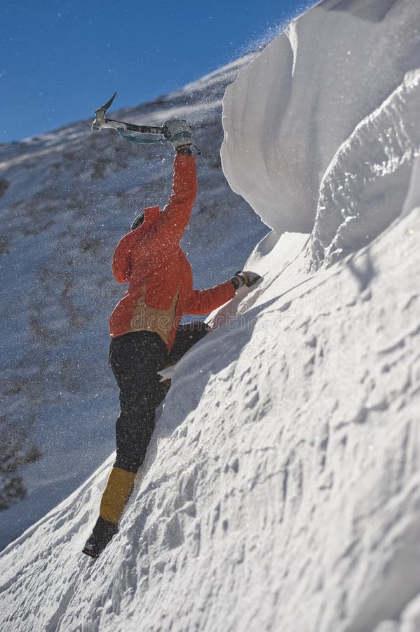 Alpinista escaladora uma cornija de neve usando machados de gelo através da neve soprada pelo vento forte.