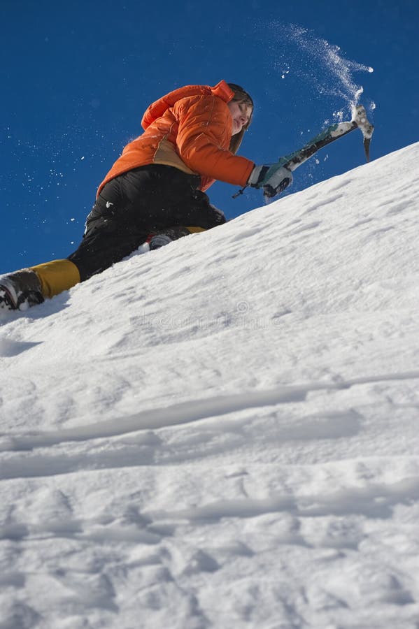 Alpinista escaladora uma cornija de neve usando machados de gelo através da neve soprada pelo vento forte.
