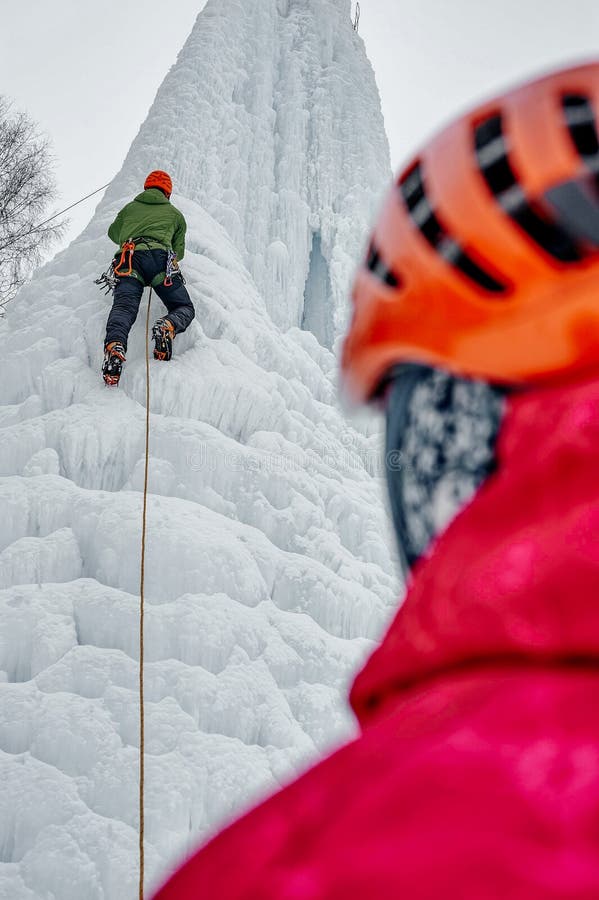Alpinistisch man met ijsgereedschappen bijl in oranje helm die een ijslaag beklimt stock afbeelding Alpinistisch man met ijsgereedschappen bijl in oranje helm die een ijslaag beklimt stock afbeelding