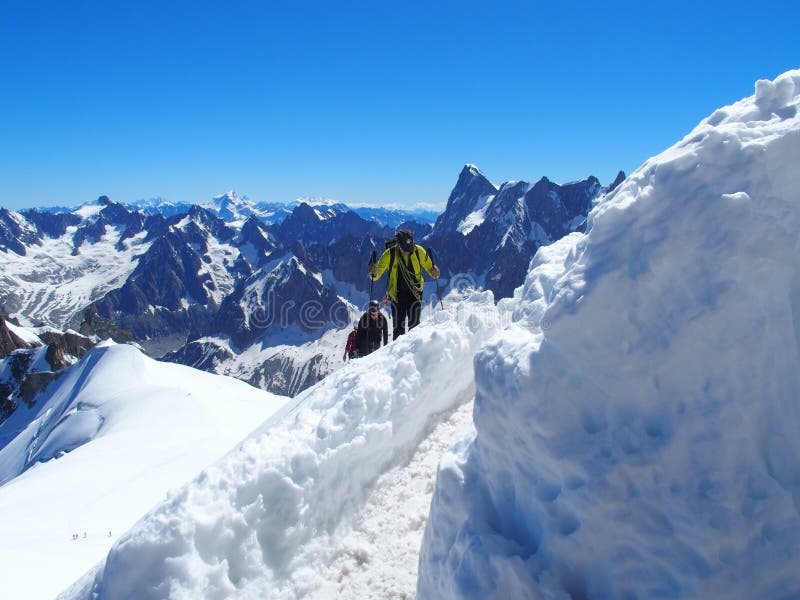 Alpinists and mountaineer climber in french ALPS on high alpine mountains range landscape on AIGUILLE DU MIDI at CHAMONIX MONT BLANC in FRANCE with clear blue sky in warm sunny summer day, EUROPE on JULY. Alpinists and mountaineer climber in french ALPS on high alpine mountains range landscape on AIGUILLE DU MIDI at CHAMONIX MONT BLANC in FRANCE with clear blue sky in warm sunny summer day, EUROPE on JULY.