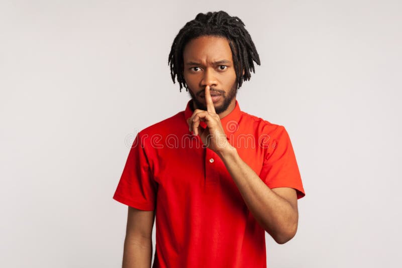 Please, be quiet. Man wearing red casual style T-shirt, holding finger on lips making hush silence gesture, asking to keep secret, don`t speak. Indoor studio shot isolated on gray background. Please, be quiet. Man wearing red casual style T-shirt, holding finger on lips making hush silence gesture, asking to keep secret, don`t speak. Indoor studio shot isolated on gray background