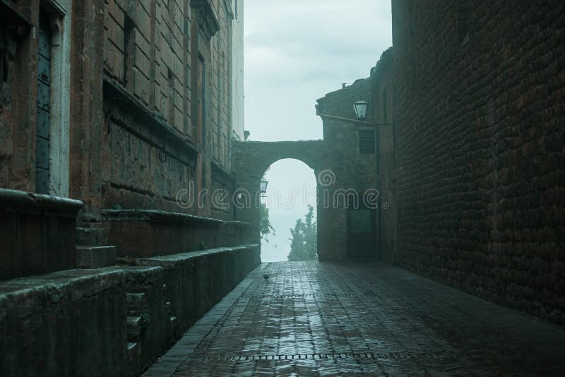 Old European narrow empty street of a medieval town at a foggy evening. Pienza, Italy. Old European narrow empty street of a medieval town at a foggy evening. Pienza, Italy