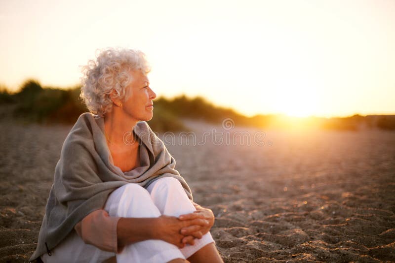 Alte Frau, die auf dem Strand weg betrachtet copyspace sitzt lizenzfreie stockbilder