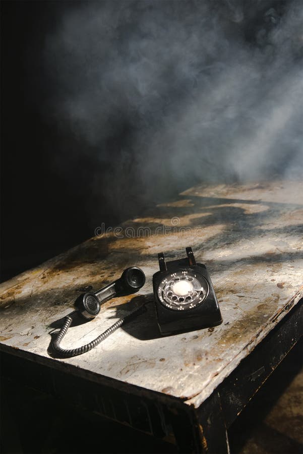 An old vintage rotary phone. The telephone is on a weathered table in a smoke filled room. An old vintage rotary phone. The telephone is on a weathered table in a smoke filled room.
