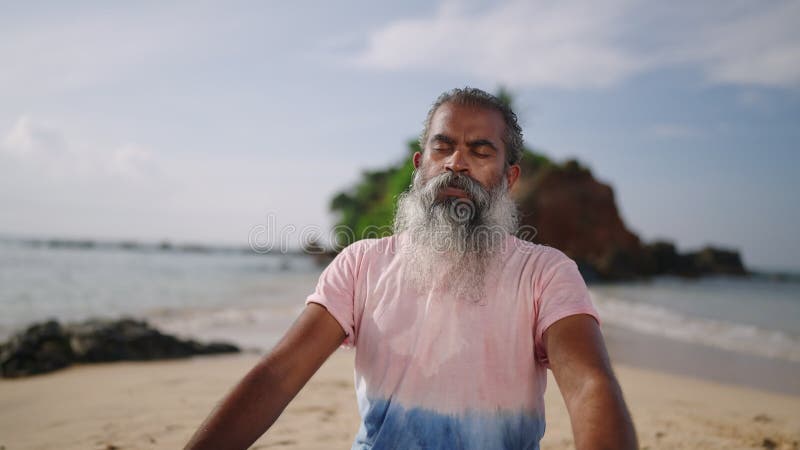 Alter Mann meditieren und sitzen in lotus posieren zum Geräusch der Wellen auf dem paradiesischen Inselstrand am Meer. schwarzes M stock video footage