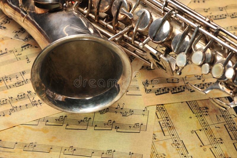 Old saxophone and notes. The Musical instrument laying on notes with classical music of the beginning of 17 centuries. Old saxophone and notes. The Musical instrument laying on notes with classical music of the beginning of 17 centuries