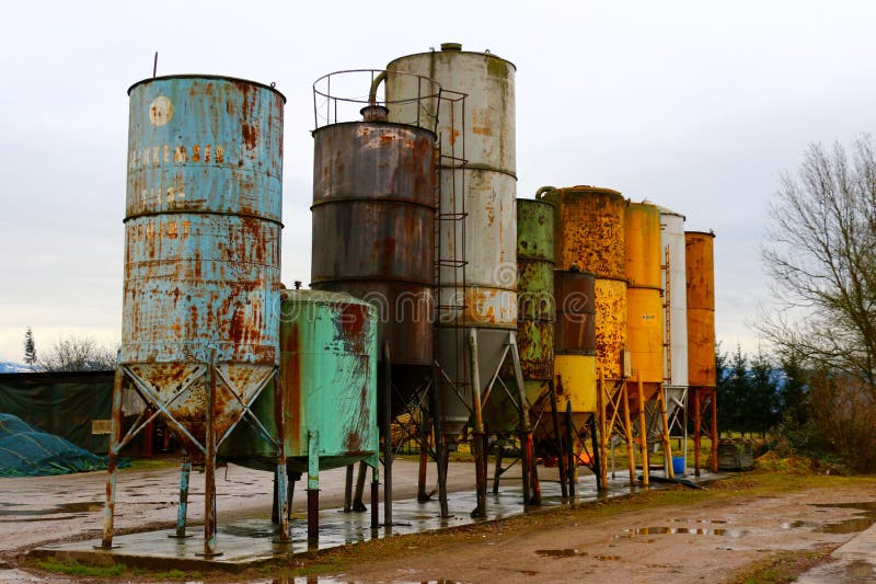 Alignment of old, rusty metal silos near a farm. Colours are blue, green, indigo, yellow, white, brown, and rust. Alignment of old, rusty metal silos near a farm. Colours are blue, green, indigo, yellow, white, brown, and rust