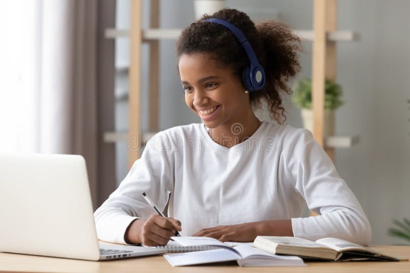 Alumno negro feliz en los auriculares que hacen la preparación de la escuela imagen de archivo