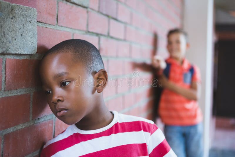 Close-up of schoolkid bullying a sad boy in corridor at school. Close-up of schoolkid bullying a sad boy in corridor at school