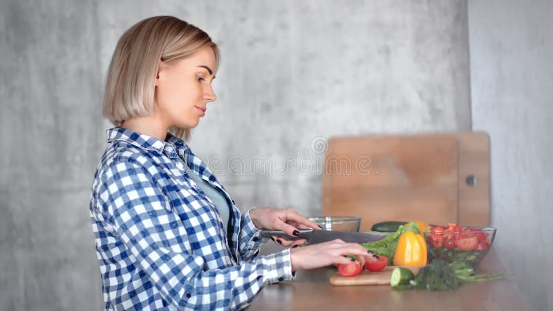 Ama de casa joven feliz agradable que cocina la comida sana que corta verduras usando vista lateral del cuchillo