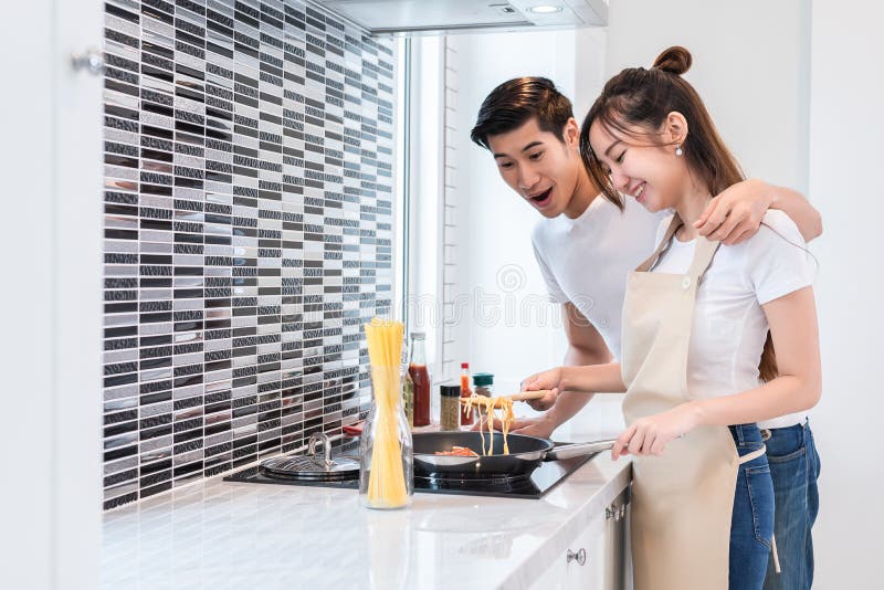 Amantes ou pares asiáticos que cozinham o jantar na sala da cozinha Ponto do homem ao alimento delicioso que fatura da mulher Fer imagens de stock royalty free Amantes ou pares asiáticos que cozinham o jantar na sala da cozinha Ponto do homem ao alimento delicioso que fatura da mulher Fer imagens de stock royalty free