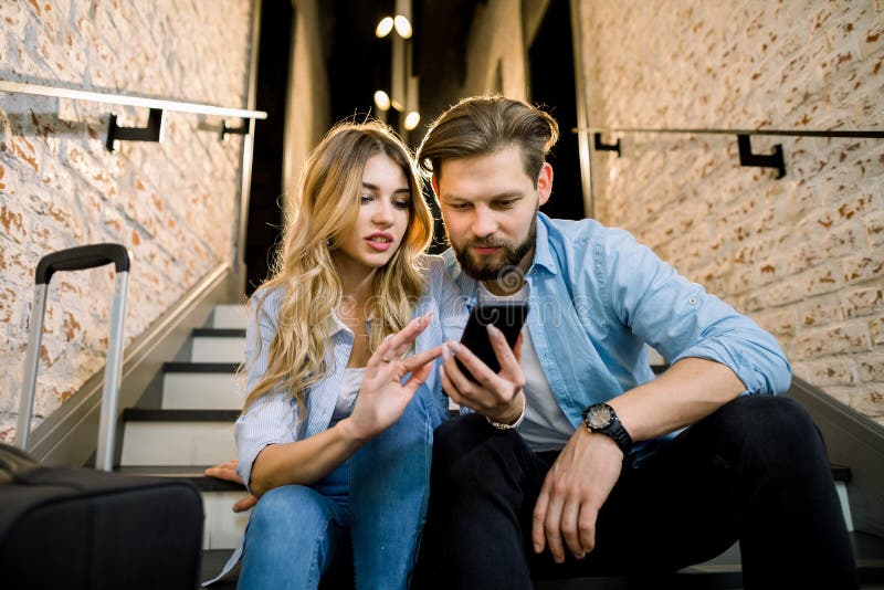 Amare una giovane coppia vestita casualmente con il cellulare, seduta sulle scale, in un elegante corridoio dell'hotel in loft immagine stock libera da diritti Amare una giovane coppia vestita casualmente con il cellulare, seduta sulle scale, in un elegante corridoio dell'hotel in loft immagine stock libera da diritti