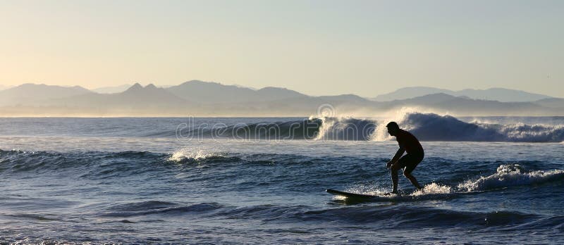 - an amateur surfer tries to catch a small wave in Byron Bay, New South Wales, Australia; breaking wave in the background