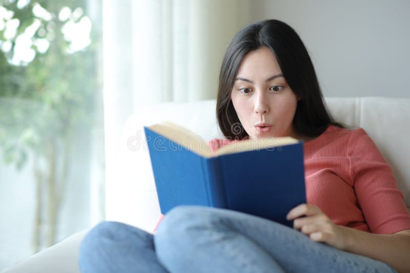 Amazed asian woman reading a book on a couch royalty free stock photos