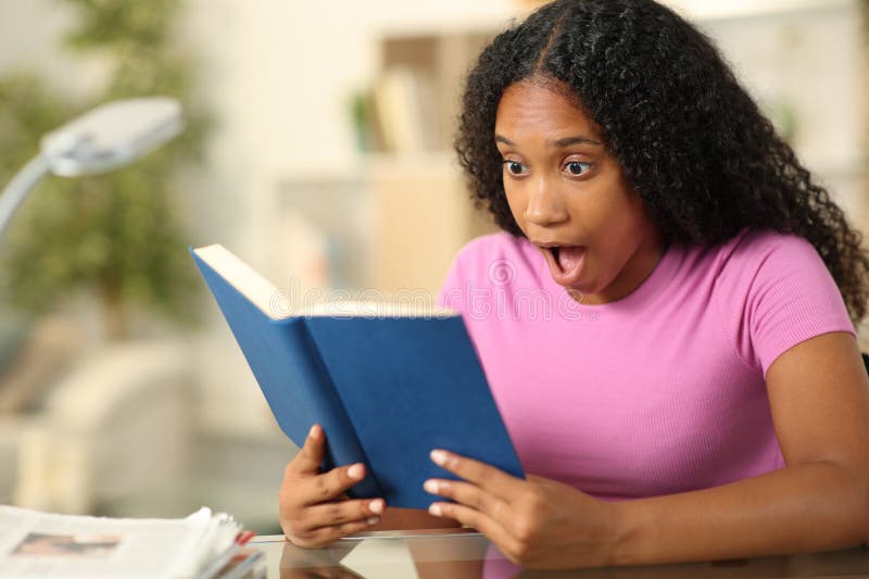 Amazed black woman reading a book at home stock images