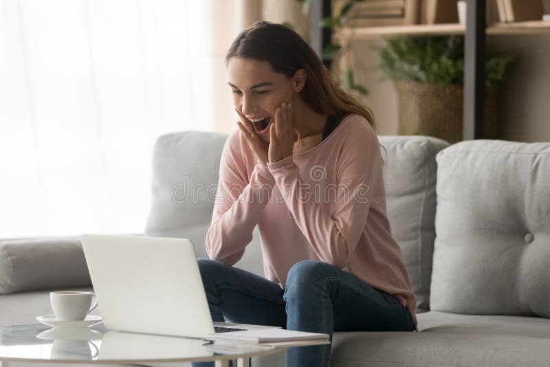 Amazed girl feeling great surprise looking at laptop at home