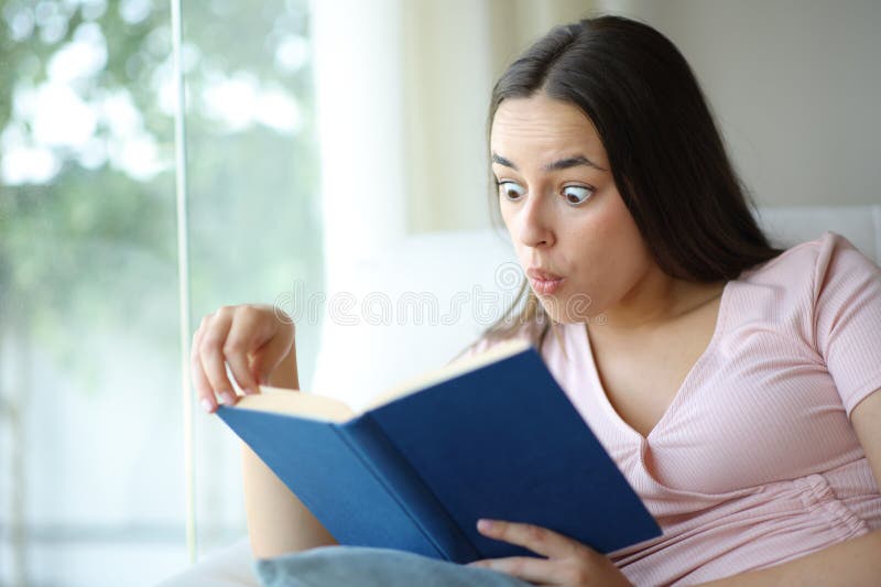 Amazed woman reading a paper book sitting in a sofa royalty free stock image