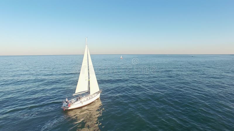 Aerial view of sail yacht sailing at sea near coastline. Blue sea with sun reflections. Drone view - birds eye angle.