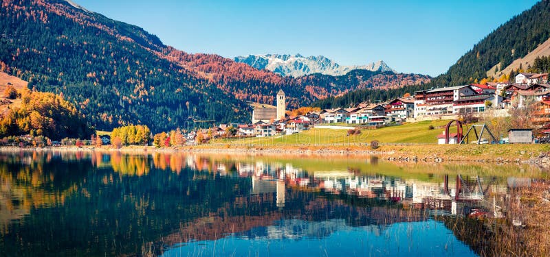 Amazing autumn panorama of Resia village and lake. Amazing morning scene of Italian Alps, South Tyrol, Italy, Europe. Traveling