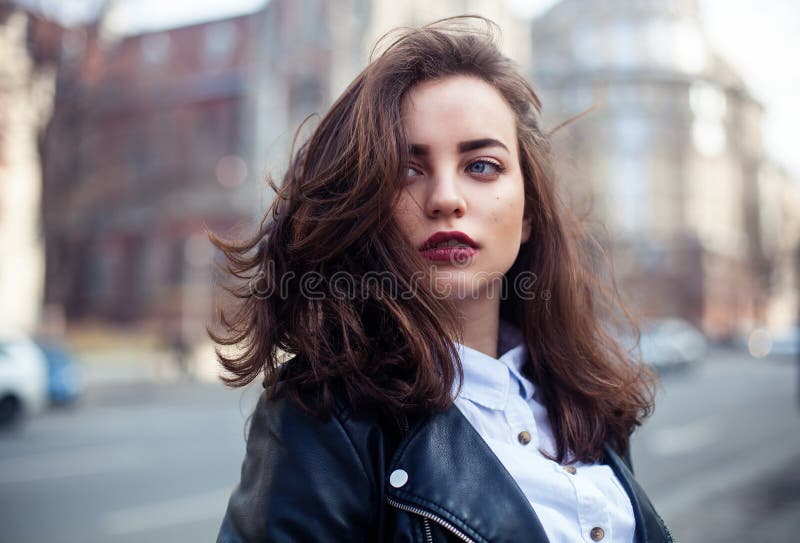 Amazing joyful pretty girl with long brunette hair. posing outdoor. leather jacket,brunette hair, bright red lips Close up fashion