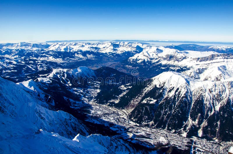 Amazing view of french town called Chamonix-Mont-Blanc. All around the summits of Alps covered with snow. Photographed from the top of Aiguille du Midi. Winter holiday in Chamonix-Mont-Blanc during sunny day. Best place for winter holiday, skiing and snowboarding.