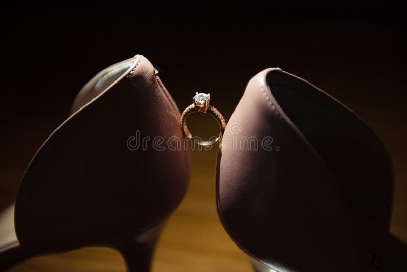 Amazing wedding engagement ring between bride`s wedding shoes close up. Women`s shoes on a dark wooden background