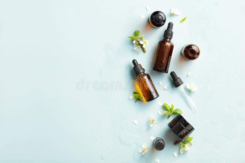 Amber glass cosmetic bottles mockups with water drops and spring flowers on blue background. Natural organic beauty