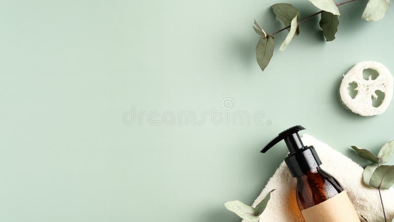 Amber glass dispenser bottle with shower gel, loofah, eucalyptus leaves on green background. Top view with copy space. Beauty