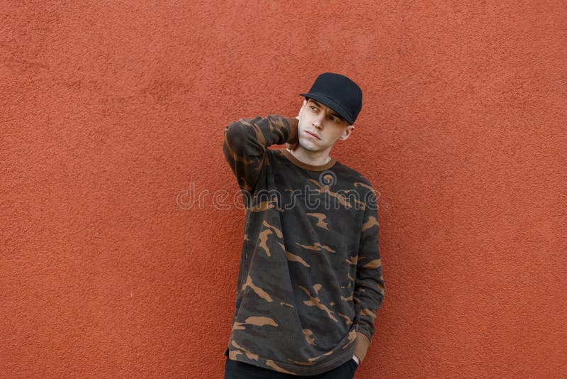 American cool young man in a fashionable cap in a green military shirt in jeans posing near a vintage wall pantone color 2019 stock photo American cool young man in a fashionable cap in a green military shirt in jeans posing near a vintage wall pantone color 2019 stock photo