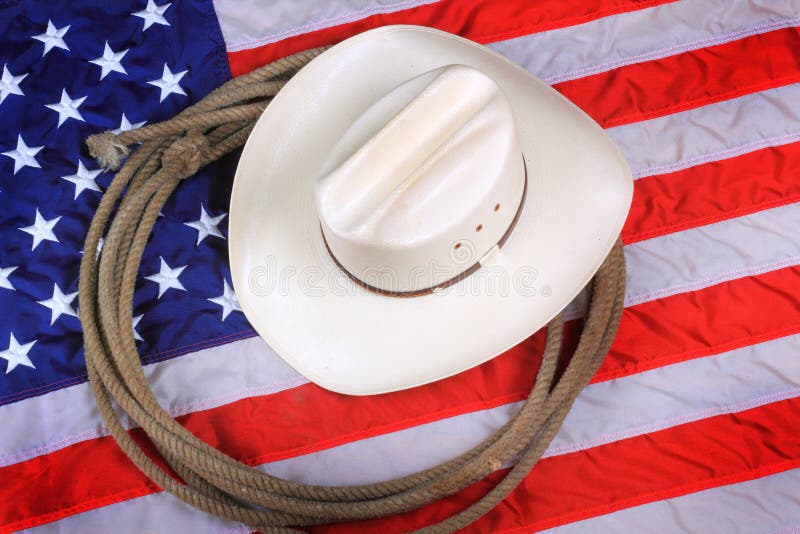 A white straw cowboy hat and rope laying on an American flag background. Symbol concept. A white straw cowboy hat and rope laying on an American flag background. Symbol concept